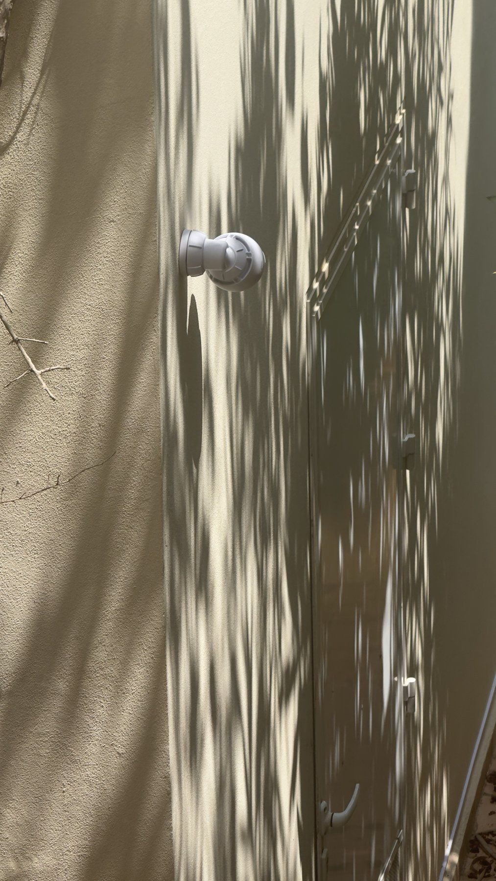 Kleine weiße Kamera an einer Hauswand im Schatten von Palmenblättern