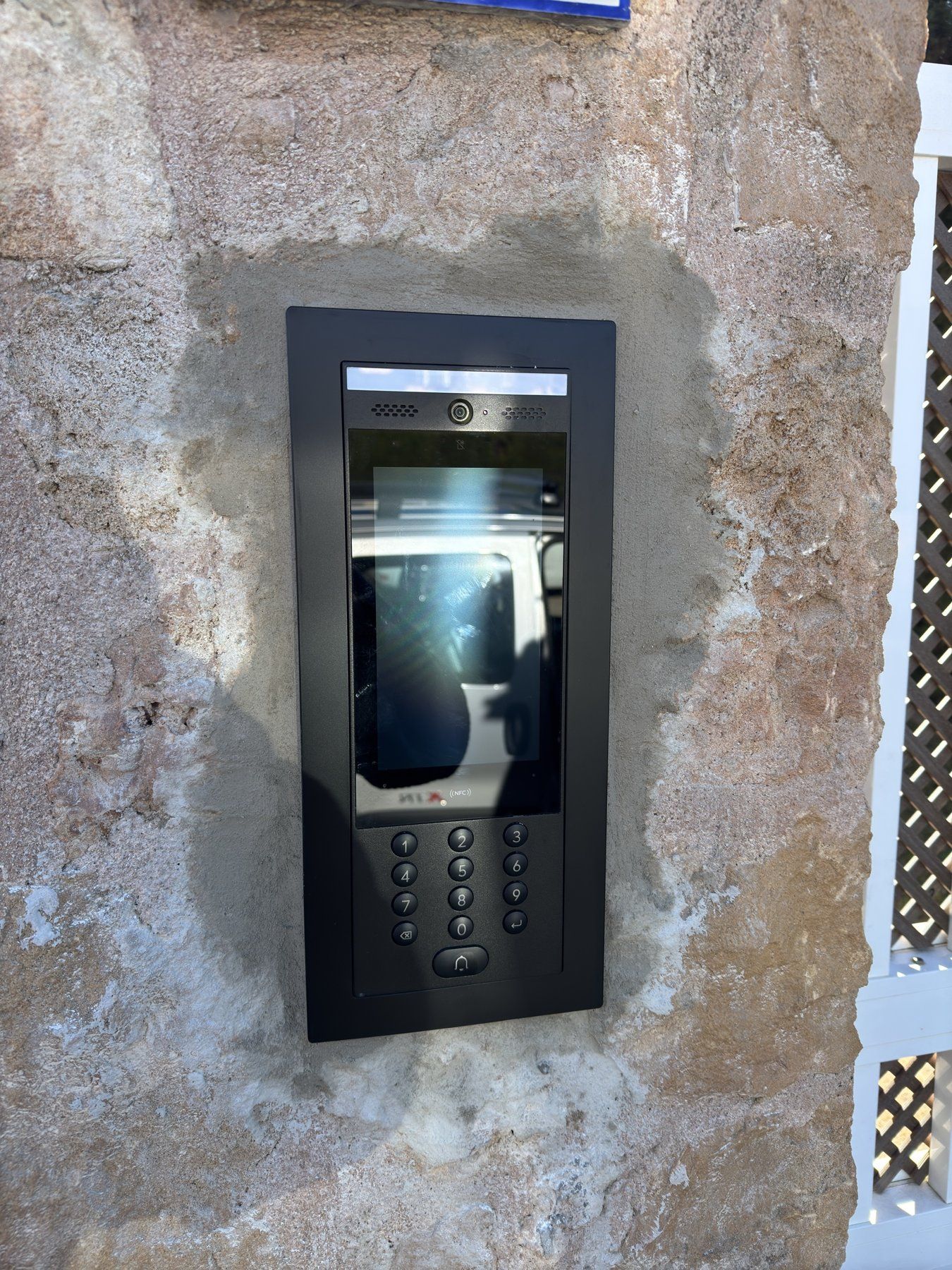 UniFi-Access-Türsprechanlage mit Bildschirm und Tastenfeld, eingebaut in eine Natursteinmauer