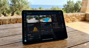 JumpIT UNIFI Ein Tablet auf einem Holztisch zeigt ein Home Assistant Mallorca Smart Home Control Dashboard f&uuml;r Poolstatus, Solarproduktion, Klima und Beleuchtung - perfektes Smart Home & Sicherheit f&uuml;r Ihre Finca mit Meerblick und &uuml;ppigem Gr&uuml;n im Freien.